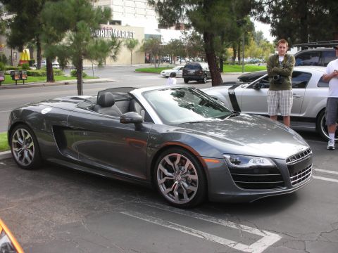 1998 Ford Crown Victoria - A gray Audi R8 convertible is parked in a lot with another car and two people standing around.