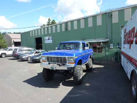 1981 Kenworth W900A - A lifted blue 1978 Ford Bronco with a winch is parked outside a commercial building next to a white truck.