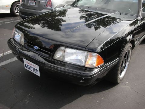 1998 Ford Crown Victoria - The front of a black Ford Mustang is shown, with a California license plate. Another vehicle is visible in the background.