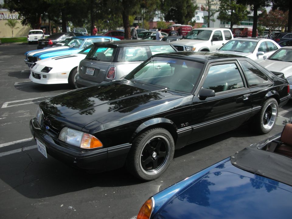 Black Ford Mustang coupe with aftermarket wheels, parked in a lot