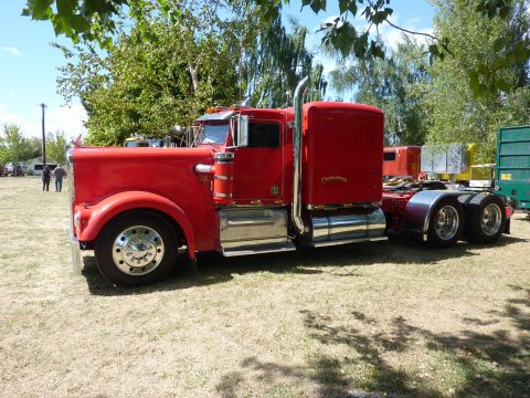 1981 Kenworth W900A - A bright red semi-truck is parked outdoors on a sunny day, with other vehicles visible in the distance.