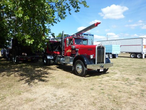 1981 Kenworth W900A - A red tow truck with a crane is parked in a field next to other trailers.