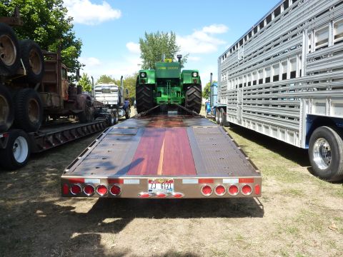 1981 Kenworth W900A - A John Deere tractor is loaded onto a flatbed trailer, parked alongside other vehicles.