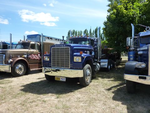 1981 Kenworth W900A - A blue Dodge truck is parked on a grassy field next to other trucks under a partly cloudy sky.