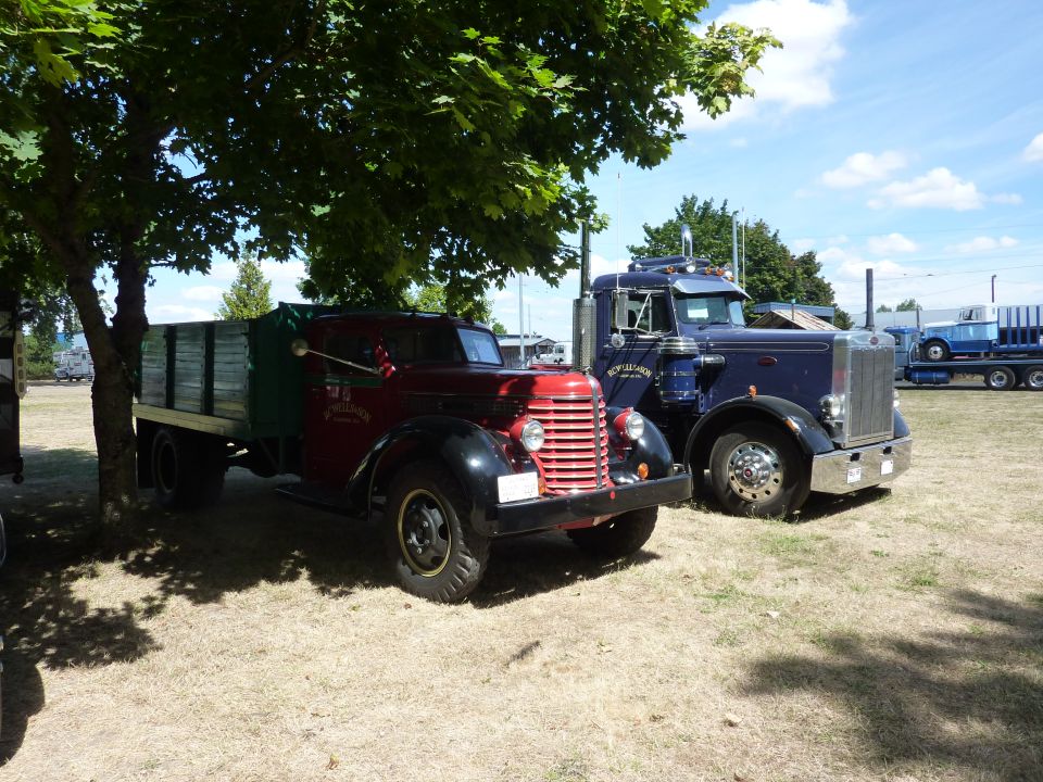 Red flatbed truck and blue semi-truck parked outdoors under a tree
