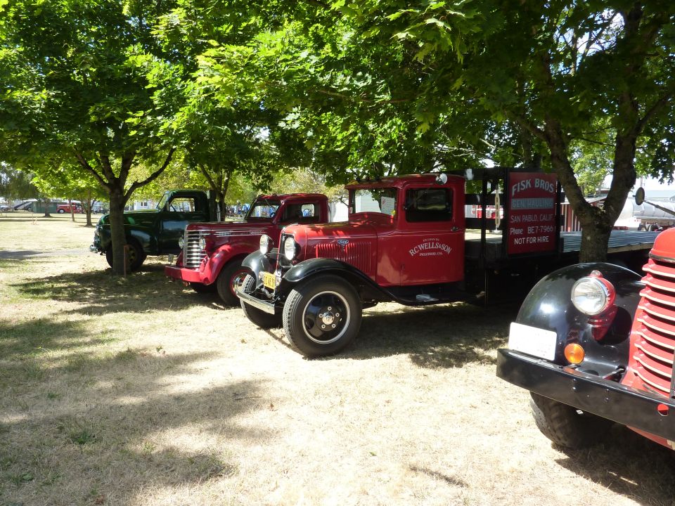 Red vintage truck with 'RC WELLSION TRADING CO.' on door, parked next to green and black trucks