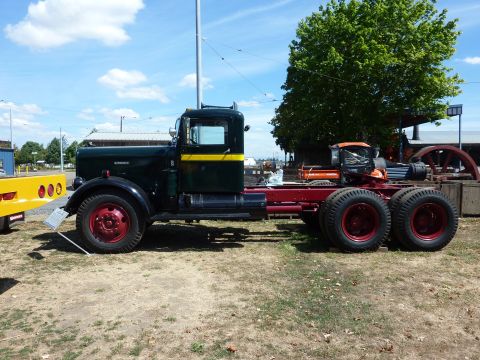 1981 Kenworth W900A - A dark green truck chassis with red wheels is parked next to a yellow trailer on a sunny day.