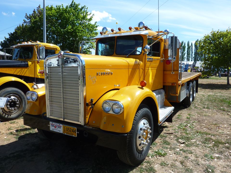 Yellow Kenworth conventional flatbed truck, front three-quarter view at a truck show