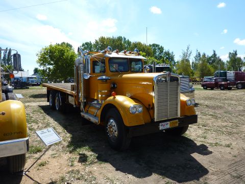 1981 Kenworth W900A - A yellow flatbed semi-truck is parked at an outdoor event with other vehicles in the background.