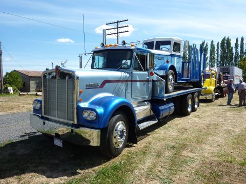 1981 Kenworth W900A - A 1981 Kenworth W900A truck transports another truck, with other vehicles and people in the background.