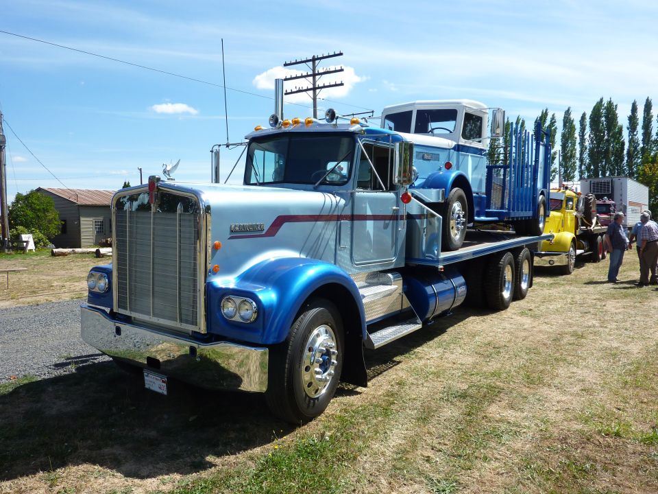 Silver and blue 1981 Kenworth W900A truck carrying a blue truck on a flatbed trailer