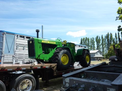 1981 Kenworth W900A - A green John Deere tractor is transported on a flatbed trailer, with a livestock trailer visible to the left.