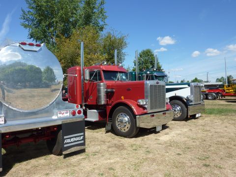 1981 Kenworth W900A - Several semi-trucks are parked in a lot on a sunny day, with a red truck and tanker trailer in the foreground.