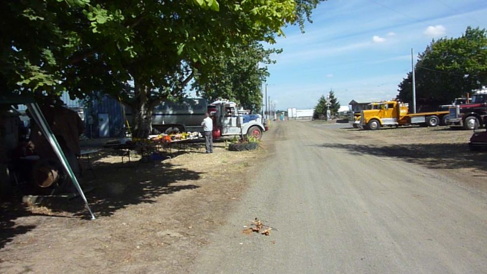 Several trucks are parked along a dirt road under trees and a blue sky