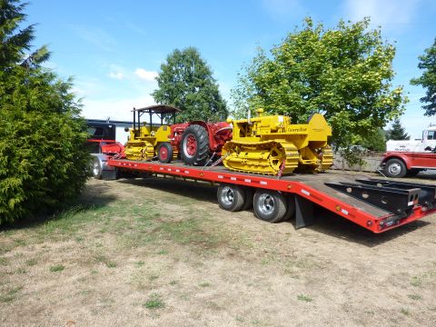 1981 Kenworth W900A - A red flatbed trailer carries two yellow bulldozers and a red tractor under a blue sky.