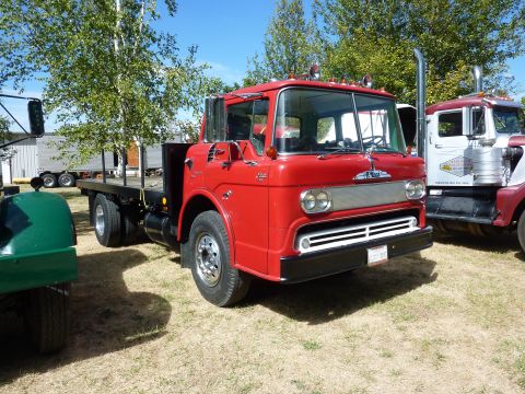 1981 Kenworth W900A - A classic red flatbed truck is parked outdoors on a sunny day, with other vehicles nearby.