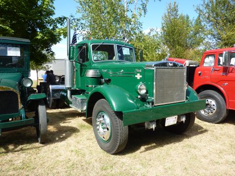 1981 Kenworth W900A - A green Mack truck is parked on a grassy field next to other vehicles.