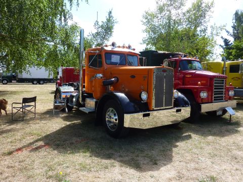 1981 Kenworth W900A - An orange semi-truck is parked next to other trucks at an outdoor event.