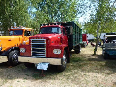 1981 Kenworth W900A - A red 1960 Dodge Crew Cab dump truck is parked at an outdoor event next to another truck.