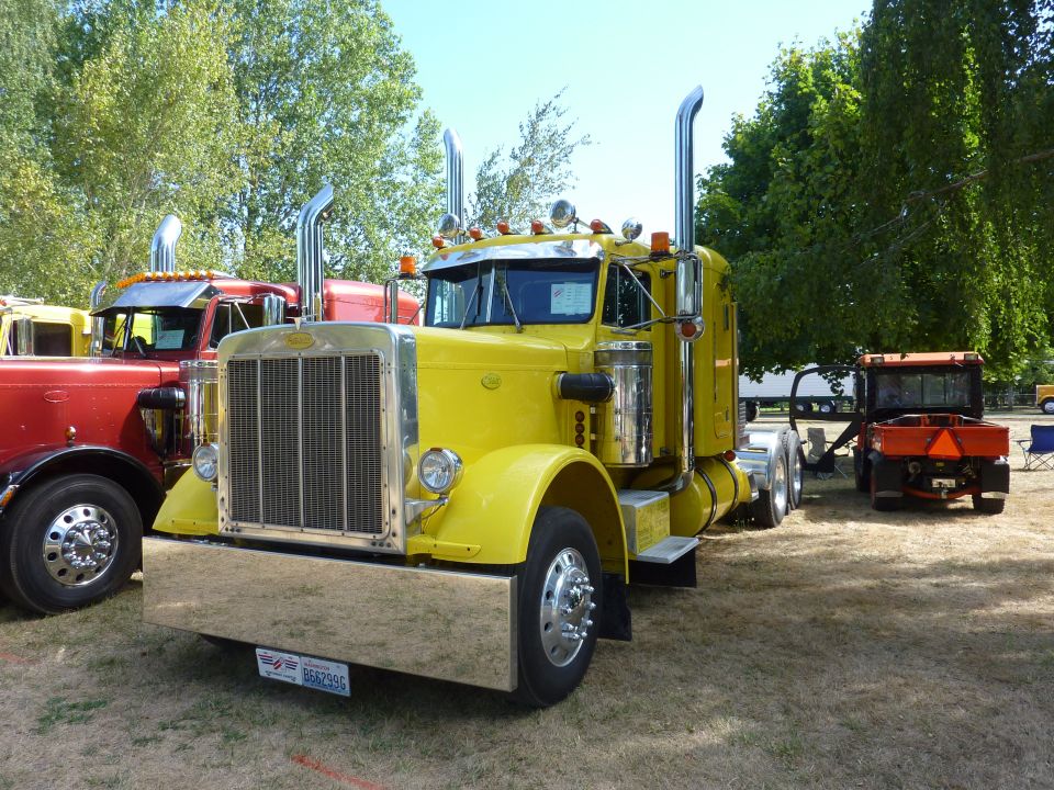 Yellow semi-truck parked next to a red truck, with a small orange tractor in the background