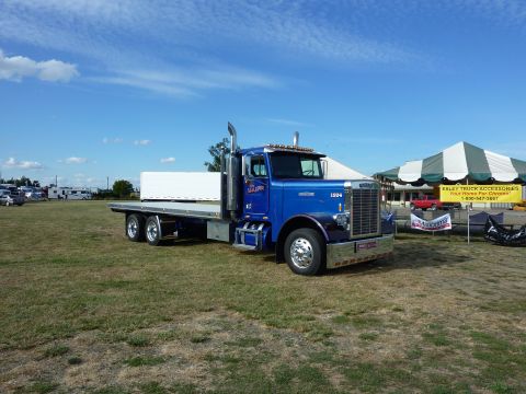 1981 Kenworth W900A - A blue flatbed semi-truck is parked on a grassy field under a clear blue sky.