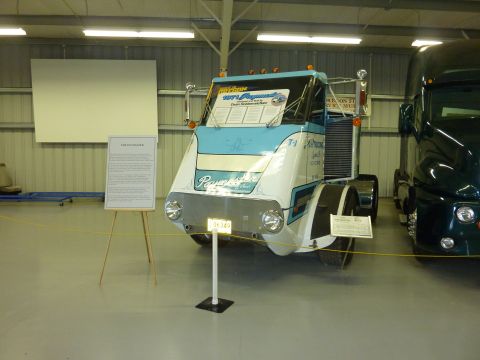 1981 Kenworth W900A - A customized semi-truck cab is displayed indoors next to another truck, with a descriptive sign nearby.