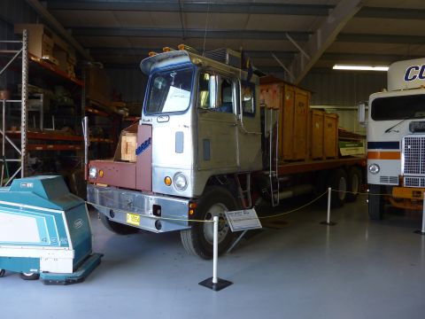 1981 Kenworth W900A - A flatbed truck is parked inside a building, with a floor scrubber and another truck nearby.