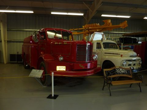 1981 Kenworth W900A - Two vintage trucks, a red FWD fire apparatus and a white Ford, are displayed indoors.