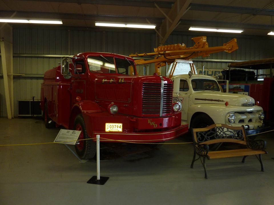 Red FWD fire truck parked next to a white Ford truck in a museum