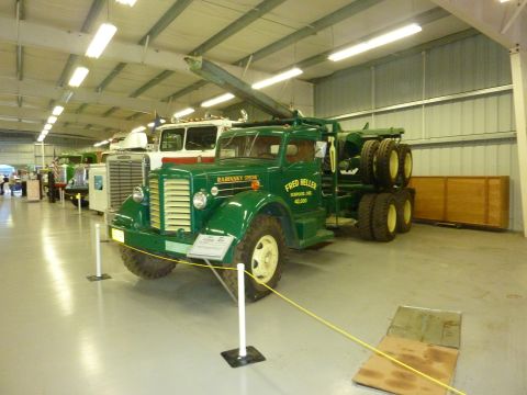 1981 Kenworth W900A - A green tow truck is displayed indoors alongside other vehicles, with signage visible on its side.
