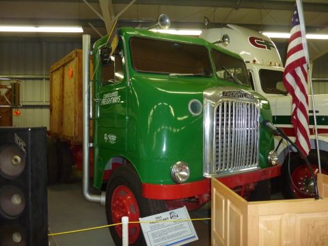 1981 Kenworth W900A - A vintage green Freightliner truck is displayed indoors, with another modern truck visible behind it.