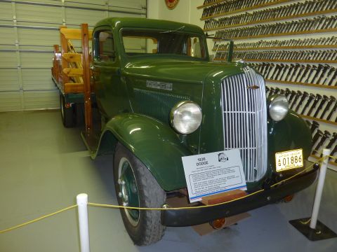 1981 Kenworth W900A - A green 1936 Dodge truck with a wooden flatbed is displayed indoors, with a sign providing details about the vehicle.