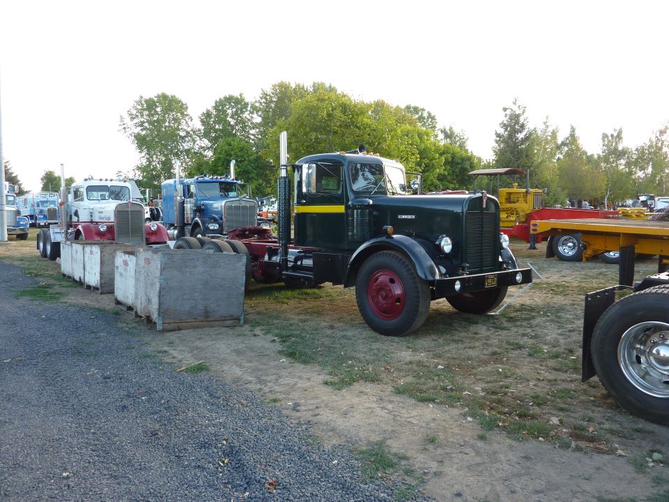 Dark green semi-truck with yellow stripe and red wheels, parked outdoors