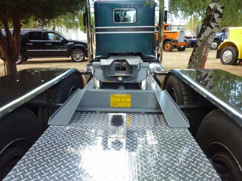 1981 Kenworth W900A - The rear chassis of a semi-truck, a fifth wheel coupling and diamond plate flooring, with other vehicles visible in the background.