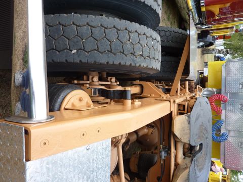 1981 Kenworth W900A - Close-up view of a yellow truck's chassis and suspension system, with other vehicles visible in the background.