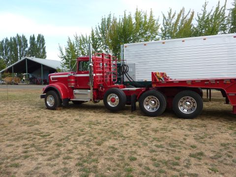 1981 Kenworth W900A - A red semi-truck is parked next to a white trailer in a grassy area with a barn in the background.