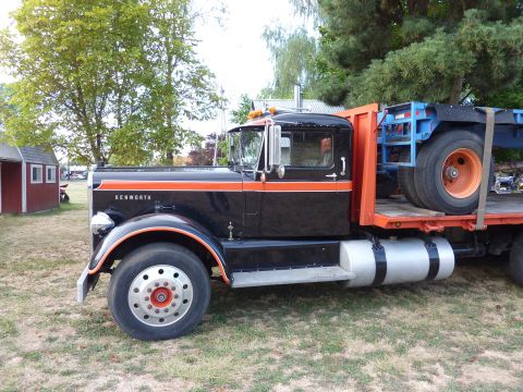 1981 Kenworth W900A - A black and orange Kenworth truck is parked on grass, with a flatbed trailer loaded with another trailer chassis.