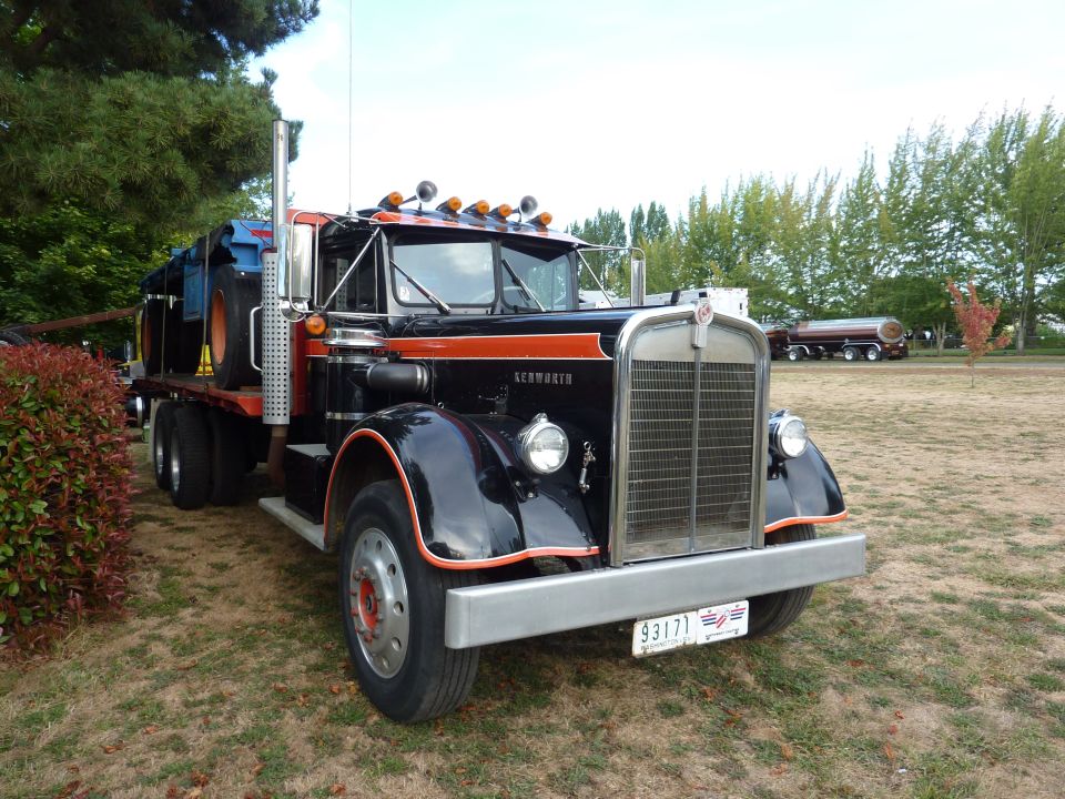 Black and orange Kenworth truck with a flatbed trailer, parked on grass