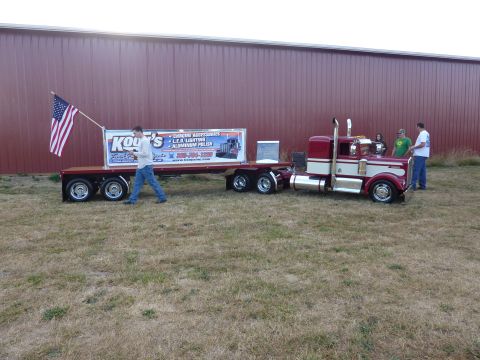 1981 Kenworth W900A - A red and white 1981 Kenworth W900A semi-truck is parked next to a trailer with an American flag and advertisement.