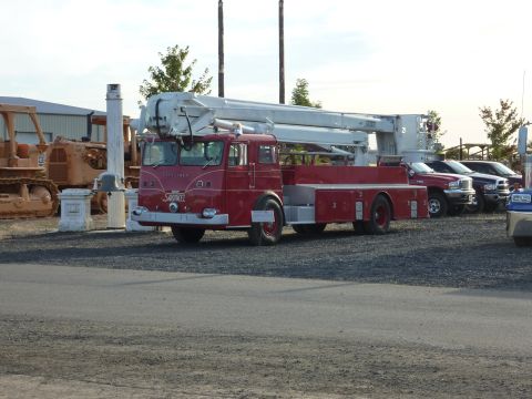 1981 Kenworth W900A - A red fire truck with a prominent white boom is parked in a lot with other vehicles and heavy machinery.