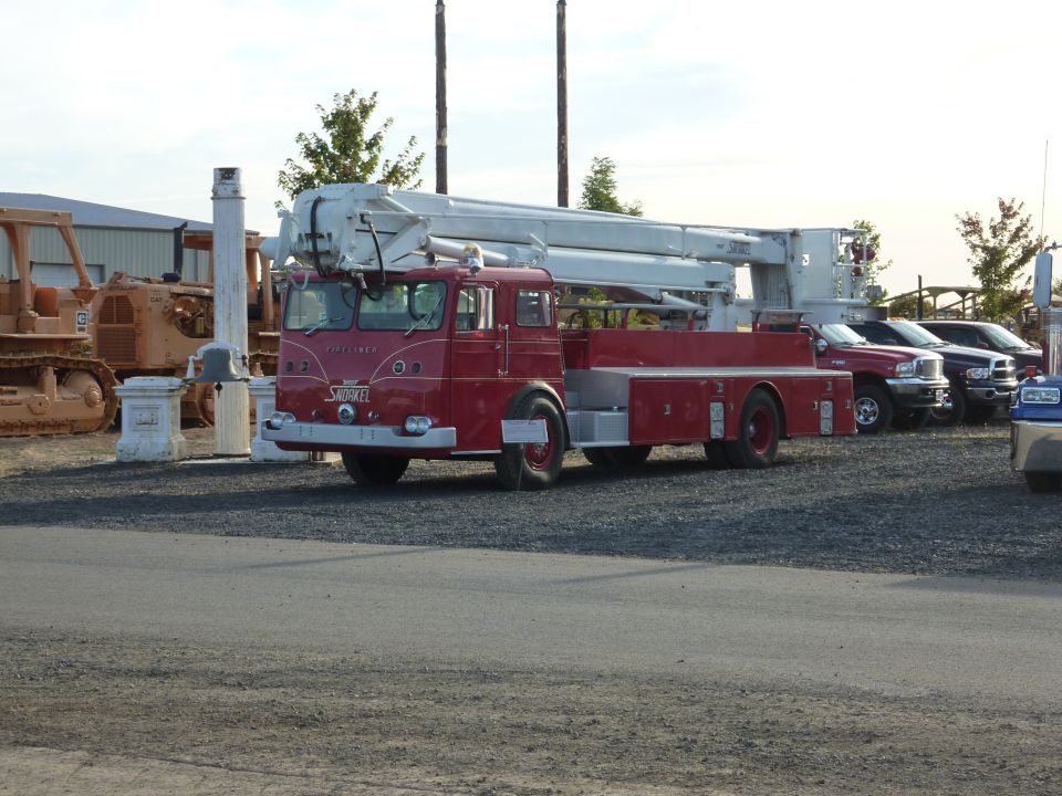 Red fire truck with white boom, parked next to other vehicles and construction equipment