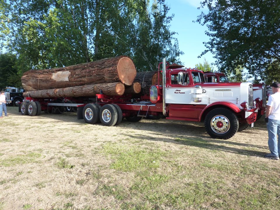 Logging truck with a trailer loaded with large logs. Another truck is visible behind it