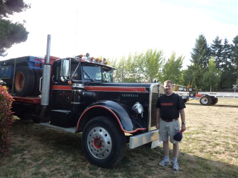 1981 Kenworth W900A - A man poses next to a black and orange Kenworth semi-truck, with a trailer visible in the background.