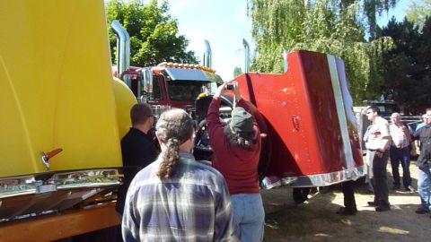 1981 Kenworth W900A - People examine two semi-trucks, one with its hood open, on a sunny day.