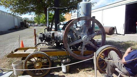 1981 Kenworth W900A - An old stationary engine sits on a trailer chassis, with large spoked wheels and a tall tank.