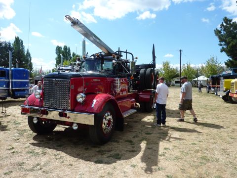 1981 Kenworth W900A - A red tow truck with a crane is parked outdoors next to other vehicles, with two men observing it.