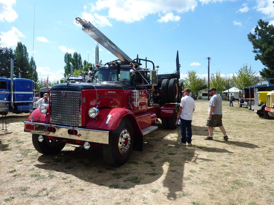 Red tow truck with a crane and two guys standing nearby. Another blue truck is to the left