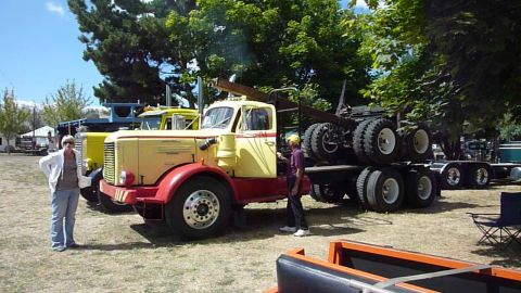 1981 Kenworth W900A - A yellow and red semi-truck is parked next to another truck, with people standing nearby.