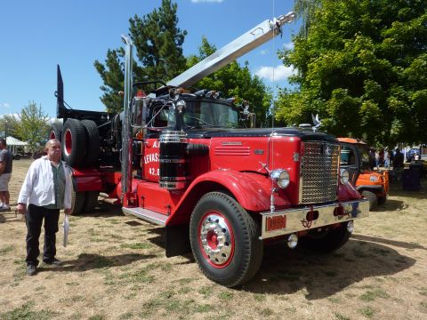 1981 Kenworth W900A - A man stands beside a vintage red tow truck with a crane attachment, parked outdoors on a sunny day.