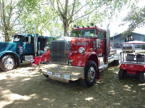 1981 Kenworth W900A - A red semi-truck is parked at an outdoor event, with another truck and a golf cart nearby.